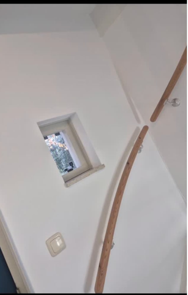 Wit geschilderde trapopgang met een houten leuning en een klein raam