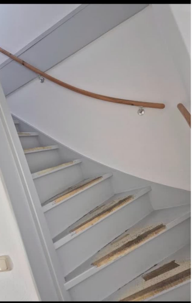 Wit geschilderde trap met houten leuning, de treden nog geschuurd